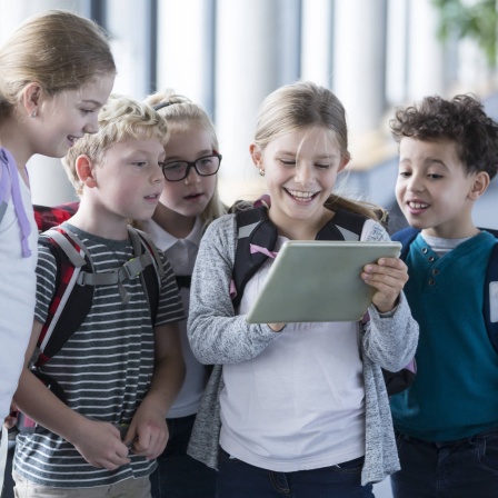 Kinder schauen im Schulkorridor in ein Tablet