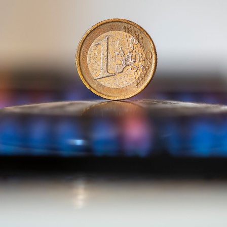 Auf dem Kochfeld eines Gasherds steht eine 1-Euro-Münze