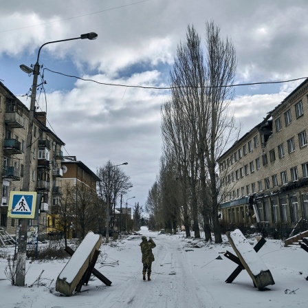 Ein ukrainischer Soldat geht eine Straße in Bachmut entlang, auf der Panzersprerren stehen.