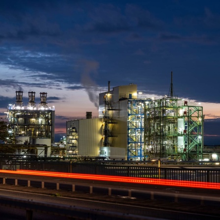 Dampf und Rauch steigen aus einer Industrieanlage im Chemiepark Wesseling im Vordergrund sind die vorbeiziehenden Rücklichter eines Autos zu sehen.