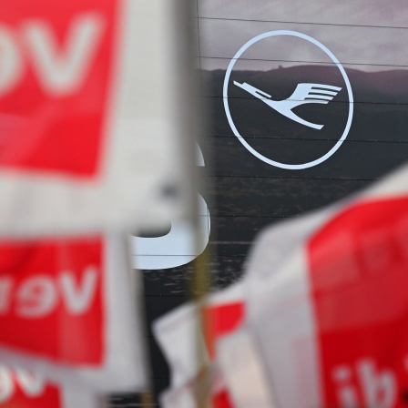 Verdi fahnen sind bei einem Streik vor einem Lufthansa Symbol zu sehen.