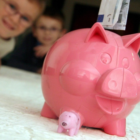 Zwei Jungs blicken auf ein pinkes Sparschwein, welches mit einem 5-Euro-Schein gefüttert wird