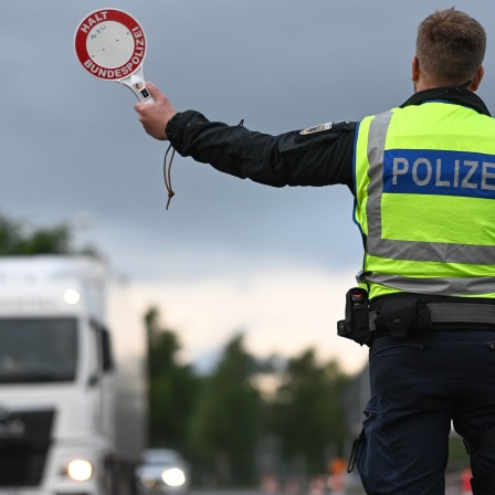 Ein Polizist mit gelber Warnweste hält auf einer Straße einen LKW an