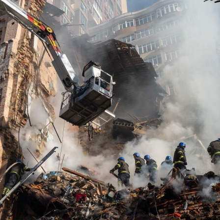 17.10.2022, Ukraine, Kiew: Feuerwehrleute arbeiten nach dem Beschuss auf Gebäude durch eine Drohne