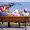 Drei Senioren sitzen auf einer Bank an der Seebrücke.