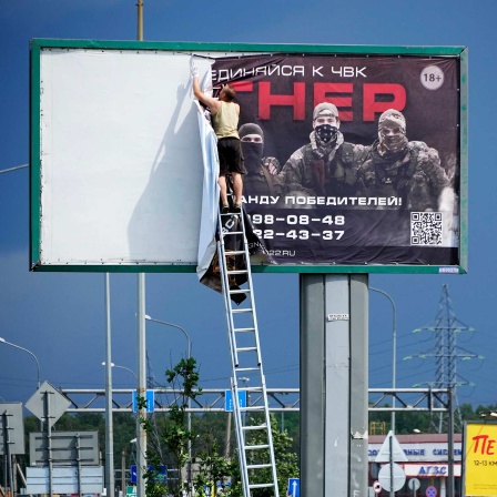 Ein Mann nimmt an einer Autobahn am Stadtrand von St. Petersburg das Plakat mit der Aufschrift "Schließt euch uns bei Wagner an" ab