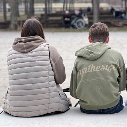 Drei Jugendliche sitzen in München in einem Park nebeneinander.