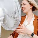 Lächelnde blonde Geschäftsfrau mit zerzaustem Haar vor einem elektrischen Ventilator