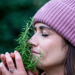 Eine junge Frau riecht mit geschlossenen Augen an einem Strauß Rosmarin