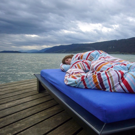 Eine Frau liegt in Decken eingehüllt auf einem Bett auf einem Bootssteg