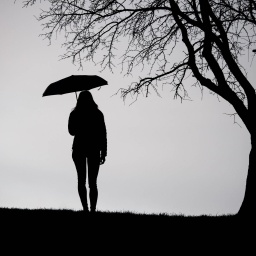 Eine Frau steht mit einem Regenschirm neben einem Baum.