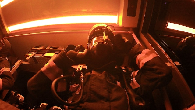 Ein Feuerwehrmann in Schutzkleidung vor einer grünen Neonröhre aus der Froschperspektive.