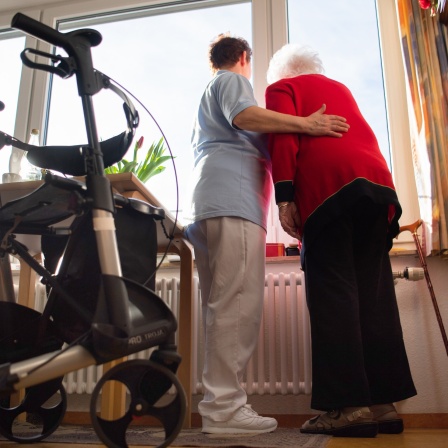 Eine Pflegerin (l) und eine Bewohnerin des Pflegeheims schauen zusammen aus einem Fenster im Wohnbereich des Pflegeheims