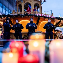 Polizisten sichern den Weihnachtsmarkt, wobei Kerzen vor ihnen brennen.