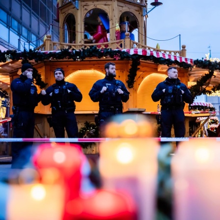 Polizisten sichern den Weihnachtsmarkt, wobei Kerzen vor ihnen brennen.