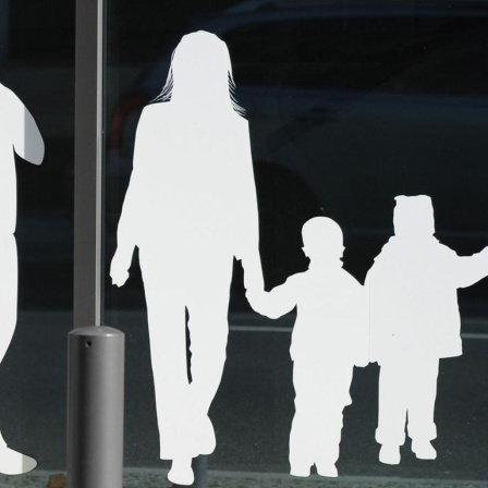 Weiße Figuren von einem Vater mit Kind und einer Familie mit Kindern kleben auf einer Glasscheibe.