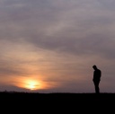 Ein Mann steht mit gesenktem Kopf im Sonnenuntergang auf einem Hügel (Symbolfoto)