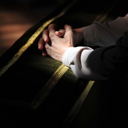 Auf einer Kirchenbank liegen die zum Gebet gefalteten Hände eines jungen Mannes.