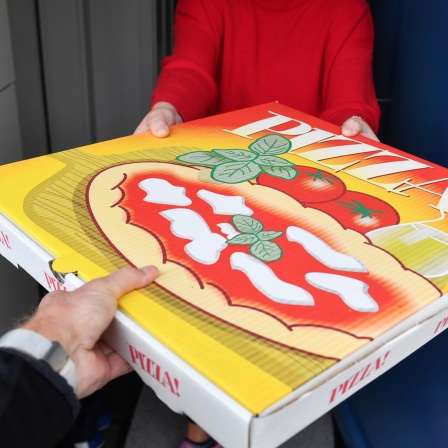 Eine Pizzaschachtel wird an der Haustür von einem Lieferdienst an eine Kundin übergeben