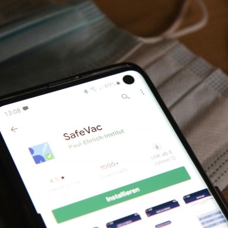 Ein Smartphone mit der App SafeVac liegt auf blauen Einwegschutzmasken.