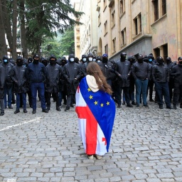 Ein Demonstrant mit drapierten georgischen National- und EU-Flaggen steht in Tiflis vor der Polizei, die den Weg zum Parlamentsgebäude blockiert.
