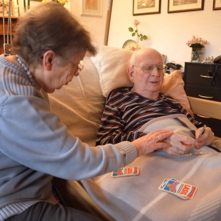 85 jähriger Demenzpatient in seinem Krankenbett versucht mit seiner 82 jährigen Ehefrau Karten zu spielen.