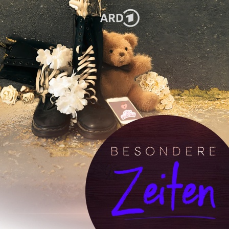 Springerstiefel, bedeckt mit weißen Blüten, daneben ein Teddybär und ein Smartphone mit einem Like-Logo auf dem Bildschirm liegen auf dem Boden vor einer grauen Wand