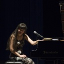 Eine Frau sitzt an einem Flügel auf einer Bühne und lächelt.