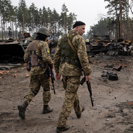 Zwei ukrainische Soldaten gehen eine Straße entlang, auf der zerstörte russische Panzer stehen