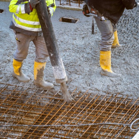 Personen mit Gummistiefel verteilen flüssigen Beton auf einem Stahlgitter