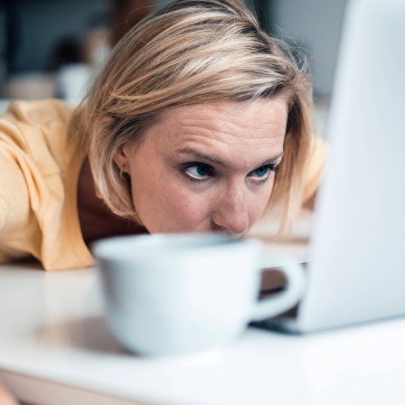 Frau liegt vor einem Laptop und schaut müde auf den Bildschirm: Wir brauchen mehr als ein Drittel unseres Gehirns, um unsere Augen zu bedienen. Wenn wir müde sind, ist unsere Sehrleistung deutlich geringer.