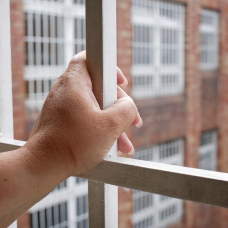 Ersatzfreiheitsstrafen werden seit Jahren kontrovers diskutiert. Zu sehen: Eine Hand umfasst das Gitter an einem Gefängnisfenster mit Blick auf einen Innenhof