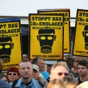 Demonstranten tragen gelbe Schilder, auf denen schwarze Gasmasken und die Aufschrift "Stoppt das CO2-Endlager" aufgedruckt sind.