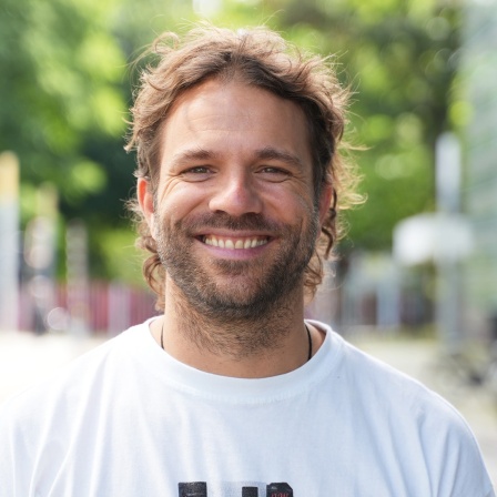 Benjamin Adrion trägt ein weißes T-Shirt und lächelt.