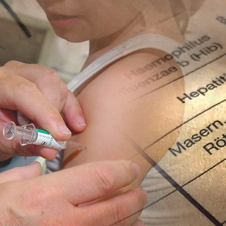 Ein Kind wird gegen Masern geimpft. Im Hintergrund sind Einträge aus einem Impfbuch zu sehen. (Bild: picture alliance / SvenSimon)s 