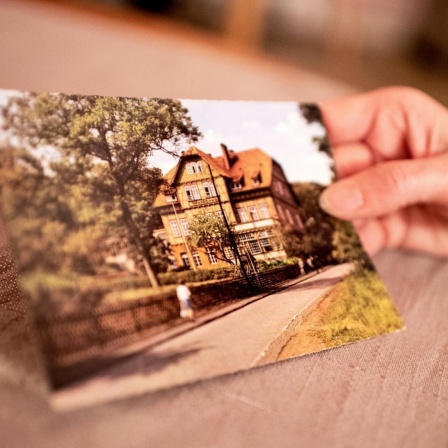 Eine Hand hält eine Postkarte mit der Ansicht der Kinderheilanstalt Waldhaus in Bad Salzdetfurth.