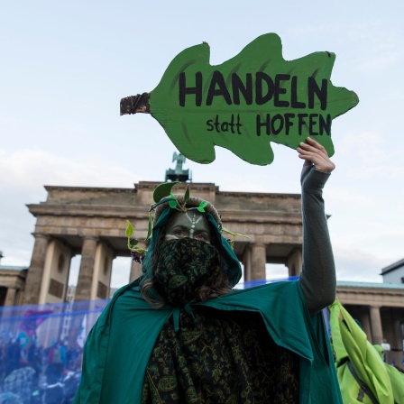 Grün verkleidete Aktivistin der Gruppe "Extinction Rebellion" hält ein Plakat in FOrm eines Eichenblattes auf dem steht "Handeln statt hoffen"