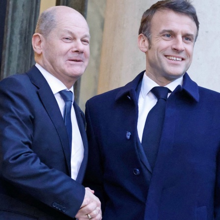 Der Präsident von Frankreich, Emmanuel Macron (Mitte), gibt Bundeskanzler Olaf Scholz (links) die Hand, als dieser im Elysee-Palast eintrifft.