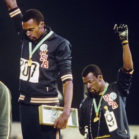 Bei der Siegerehrung für den 200m-Lauf der Männer demonstrieren die Amerikaner Tommie Smith (M, Goldmedaille) und John Carlos (r, Bronzemedaille) mit hochgereckter geballter Faust in schwarzem Handschuh für die "Black Power" Bewegung. Links der Gewinne