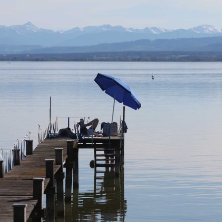 Menschen genießen unter einem Sonnenschirm auf einem Steg die sommerlichen Temperaturen am Ammersee