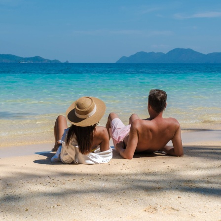 Eine Frau und ein Mann liegen am Strand mit Blick aufs Meer