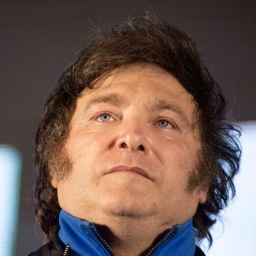 Leicht von unten fotografiertes Portrait von Javier Milei. Er trägt eine Jacke mit blauem Kragen und schaut ernst über die Kamera hinaus.