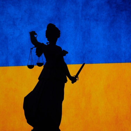 ILLUSTRATION - Die Statue der Justitia auf dem Gerechtigkeitsbrunnen steht während einer Demonstrationen der Europa Union Frankfurt gegen den Krieg in der Ukraine vor einer Ukraine-Flagge.