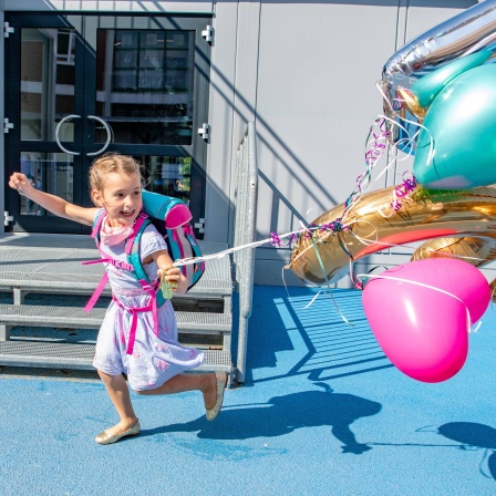 Fröhliches kleines Mädchen mit Schulranzen und Ballons