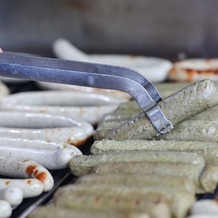 Fleischliche Bratwürste (l) und vegane Bratwürste (r) liegen nebeneinander auf dem Holzkohlengrill.