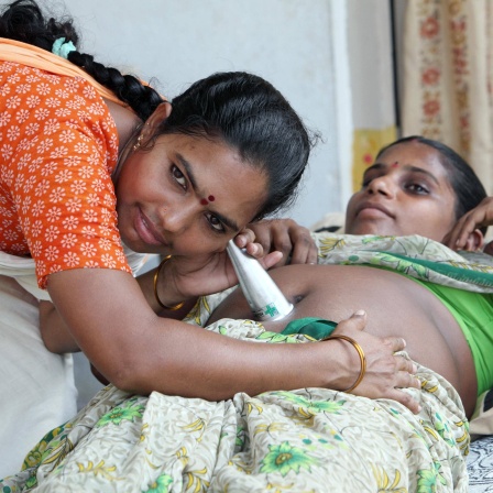 Indien - Mit einem Hebammenstethoskop horcht eine Hebamme den Bauch einer jungen Frau ab