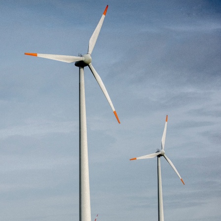 Drei Windräder stehen unter leicht bewölktem Himmel.