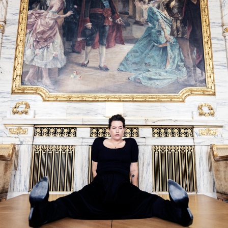 Liv Strömquist sitzt breitbeinig in schwarzen Klamotten auf dem Boden.