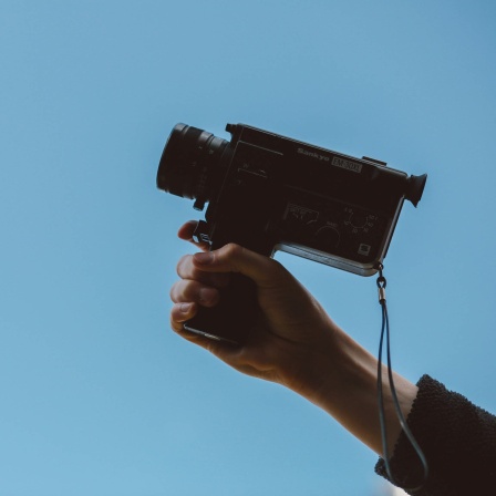 eine Hand hält eine alte Videokamera in den Himmel