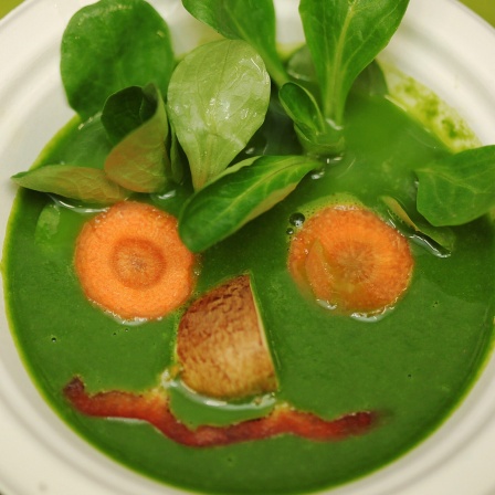 Eine vegane Spinat-Suppe, mit Feldsalat und Möhren so dekoriert, dass sie wie ein Gesicht aussieht.